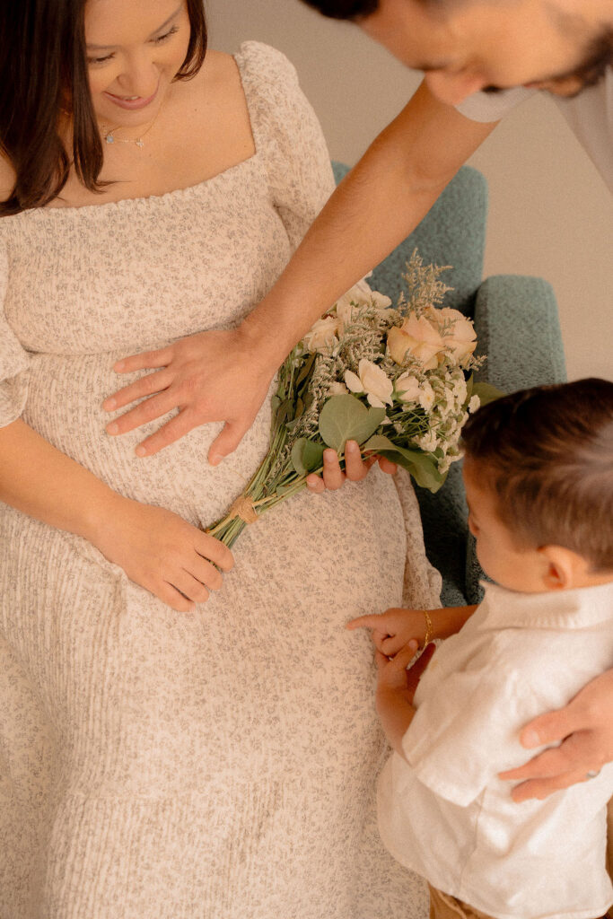 Dad touching mom's pregnant belly while holding flowers