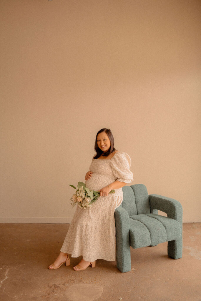 Pregnant mom sitting on a modern couch holding a gorgeous bouquet of flowers