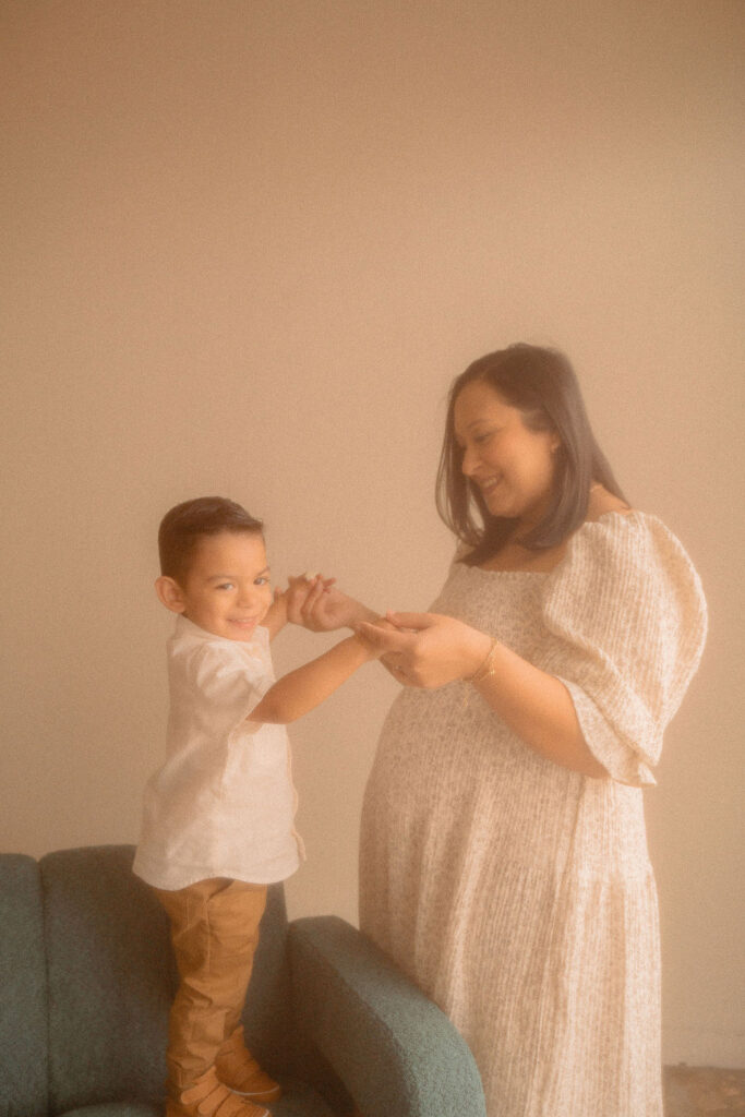 Pregnant mom dancing with her baby boy on a velvet green couch