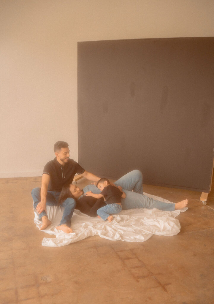 Couple dressed in denim laying down in the floor while baby son hugs mom
