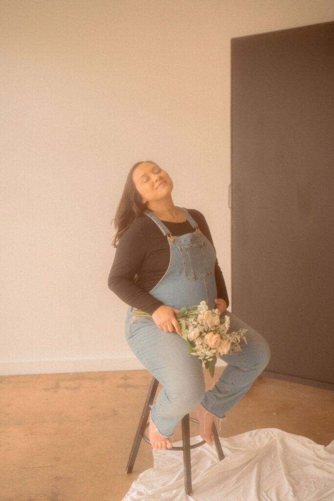 Pregnant mom sitting on a stool holding a bouquet of flowers at an indoor family session