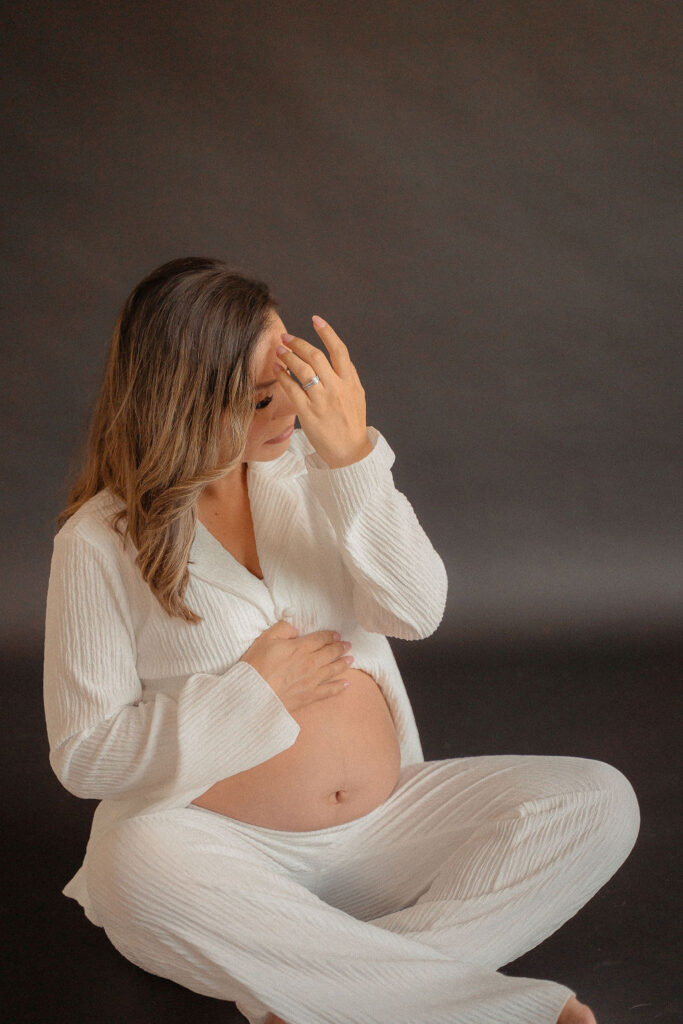 Pregnant mom sitting on the floor with white cozy outfit