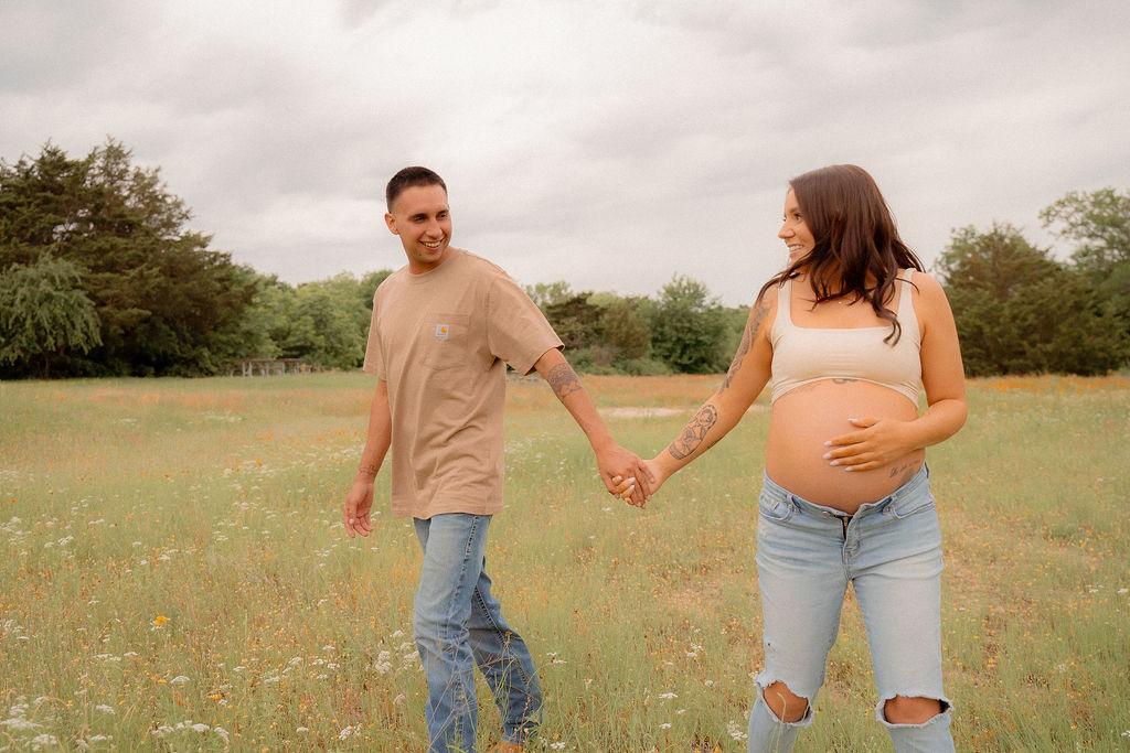 mom and dad holding hands while mom holds her belly at their fun maternity photoshoot