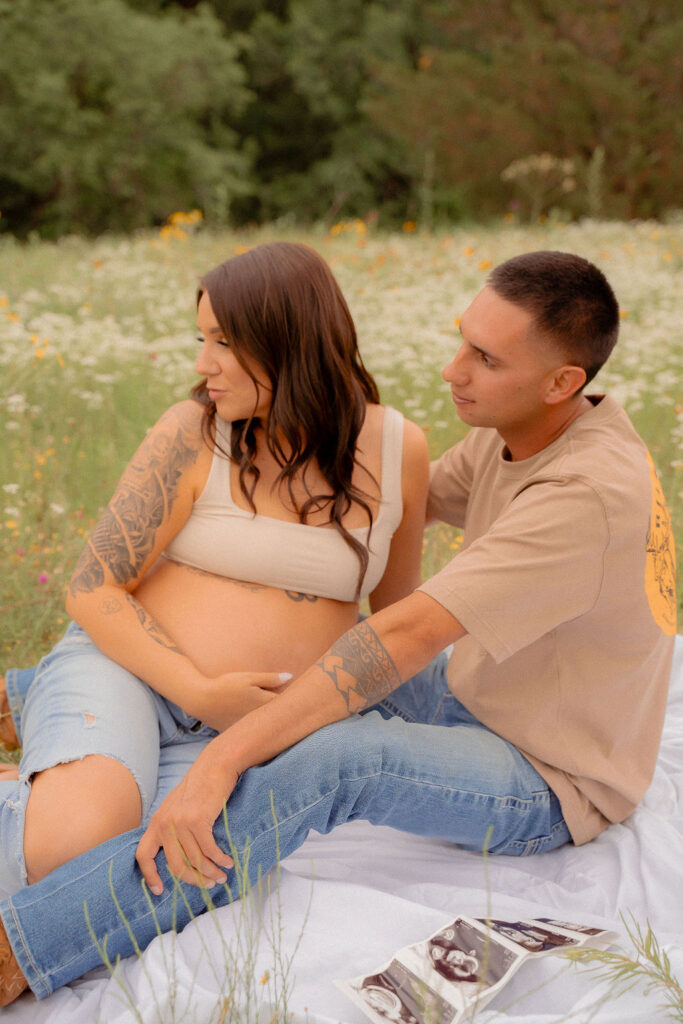 Pregnant couple sitting together starring at the wildflowers while mom holds her belly