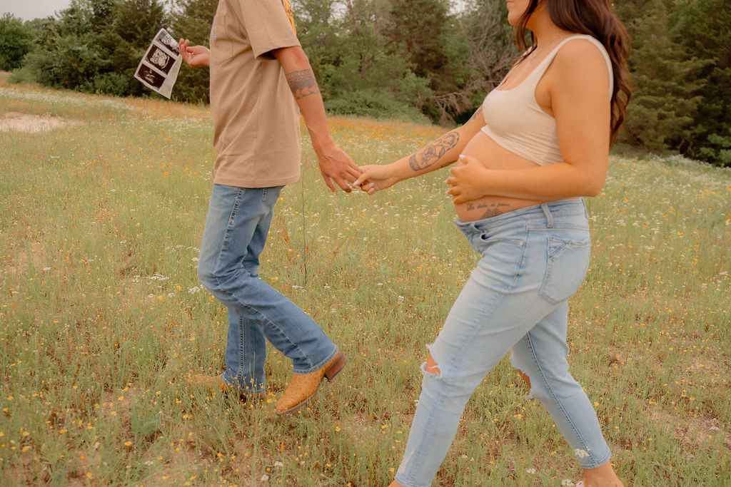 Pregnant couple walking across flower field while holding hands