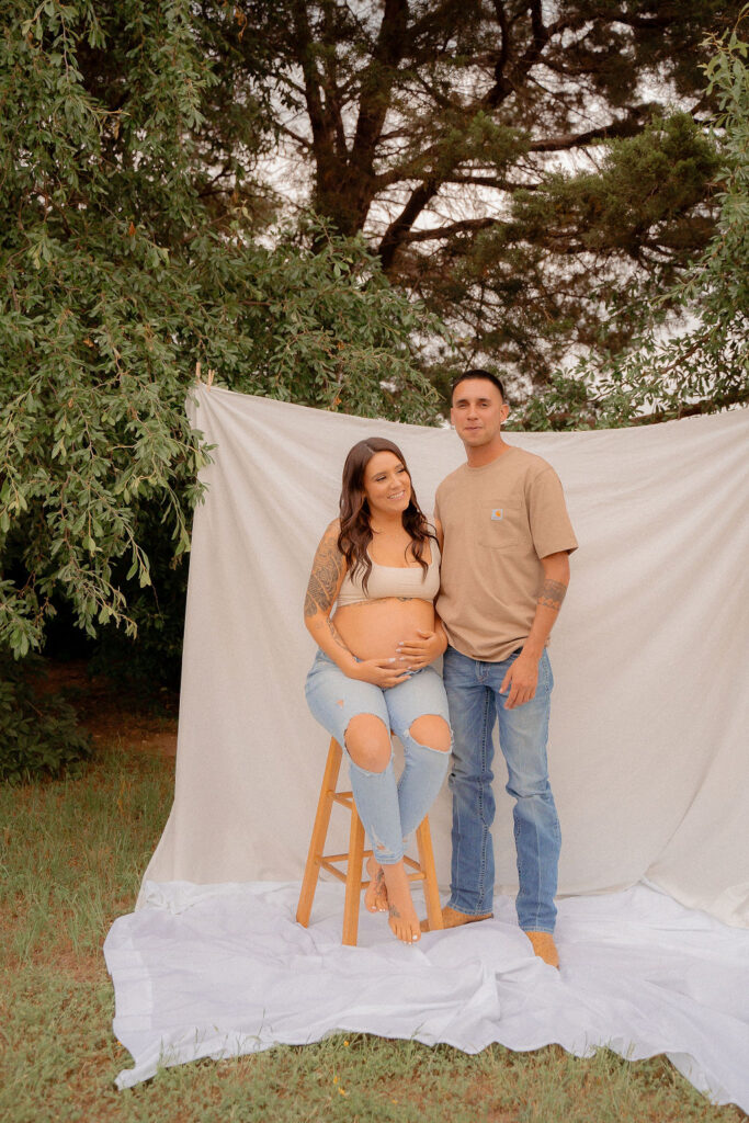 Pregnant mom sitting on a stool with dad standing next to her while they hug