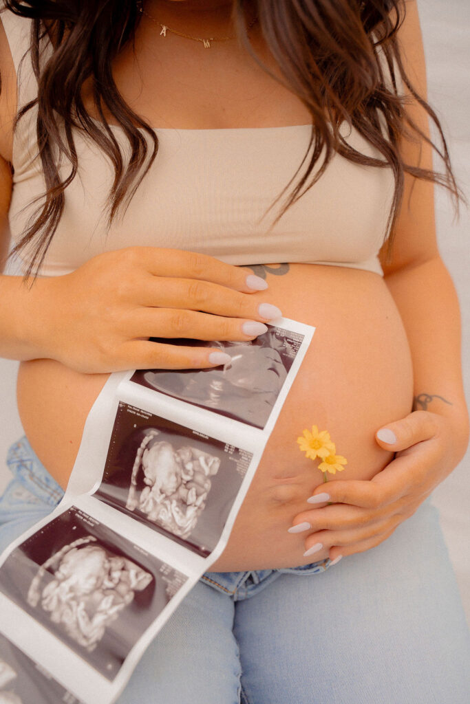 Mom holding her sonogram and yellow daisies on her belly